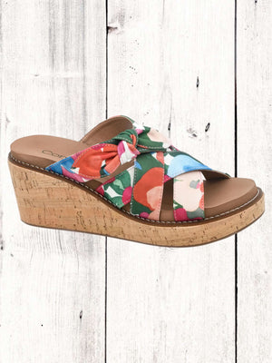A pair of Corkys(*15) Bowdacious wedge sandals with multicolored straps and cork wedge heel, displayed against a wooden background.