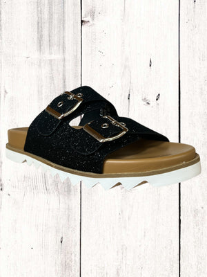 An image featuring a pair of black Corkys Dash sandals with adjustable buckles and a flat sole, displayed against a wooden background.