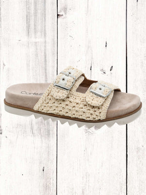 An image featuring a pair of black Corkys Dash sandals with adjustable buckles and a flat sole, displayed against a wooden background.