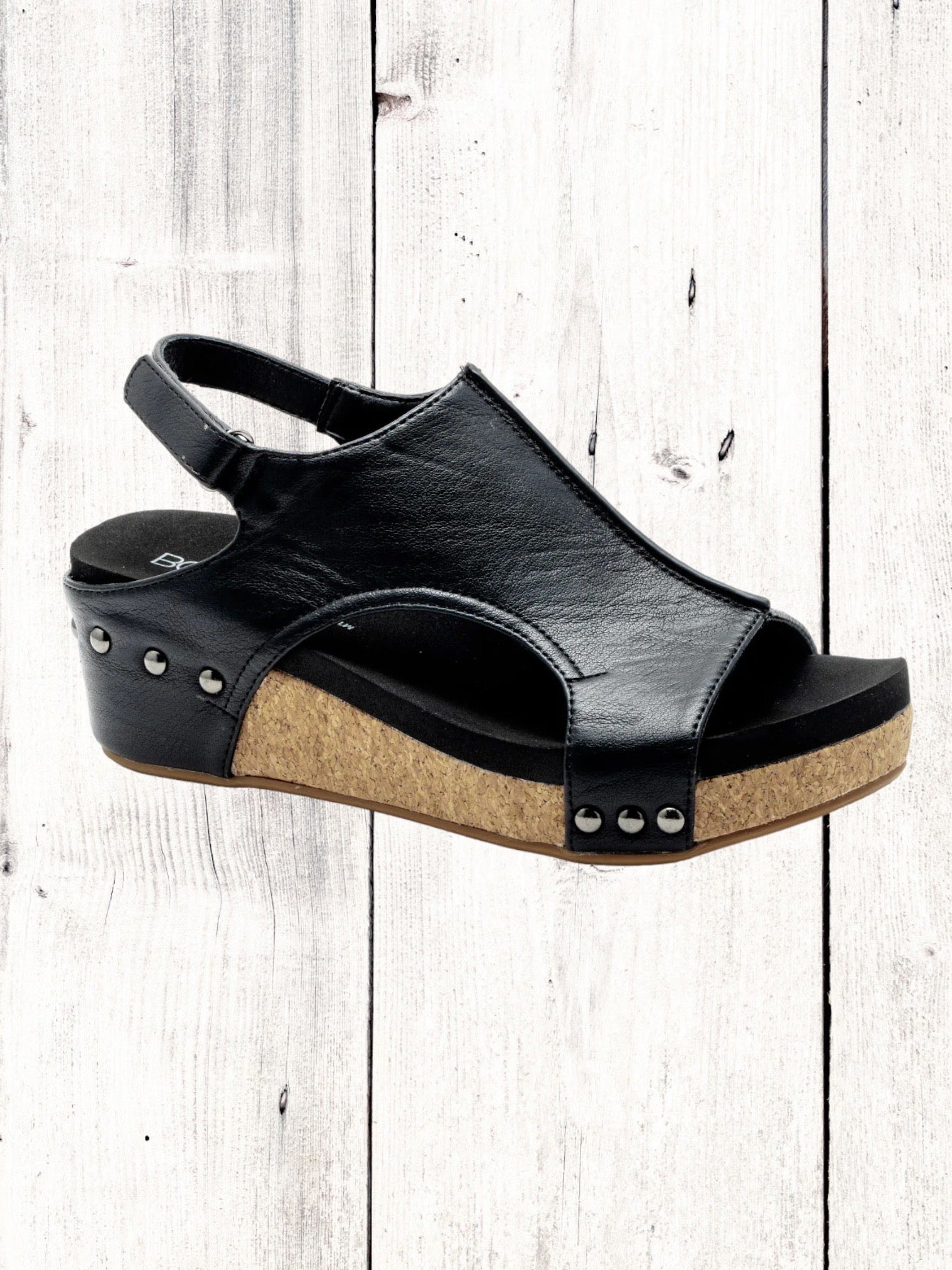 A black Corkys Volta II wedge sandal with a faux leather upper and cork wedge heel, featuring a hook and loop closure and studs on the heel.