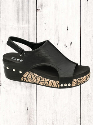 A black Corkys Volta II wedge sandal with a faux leather upper and cork wedge heel, featuring a hook and loop closure and studs on the heel.