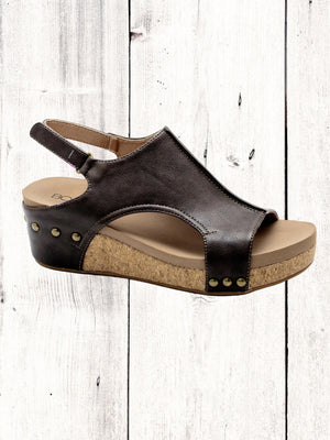 A black Corkys Volta II wedge sandal with a faux leather upper and cork wedge heel, featuring a hook and loop closure and studs on the heel.