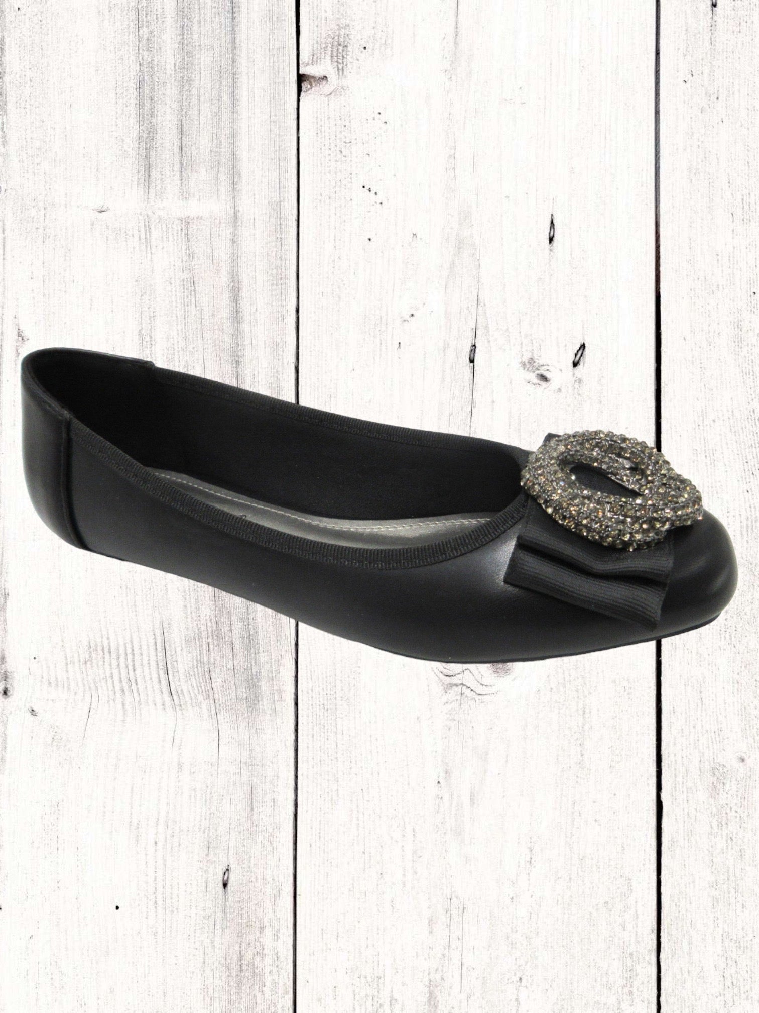 A black flat with a synthetic upper and a decorative buckle on the toe.