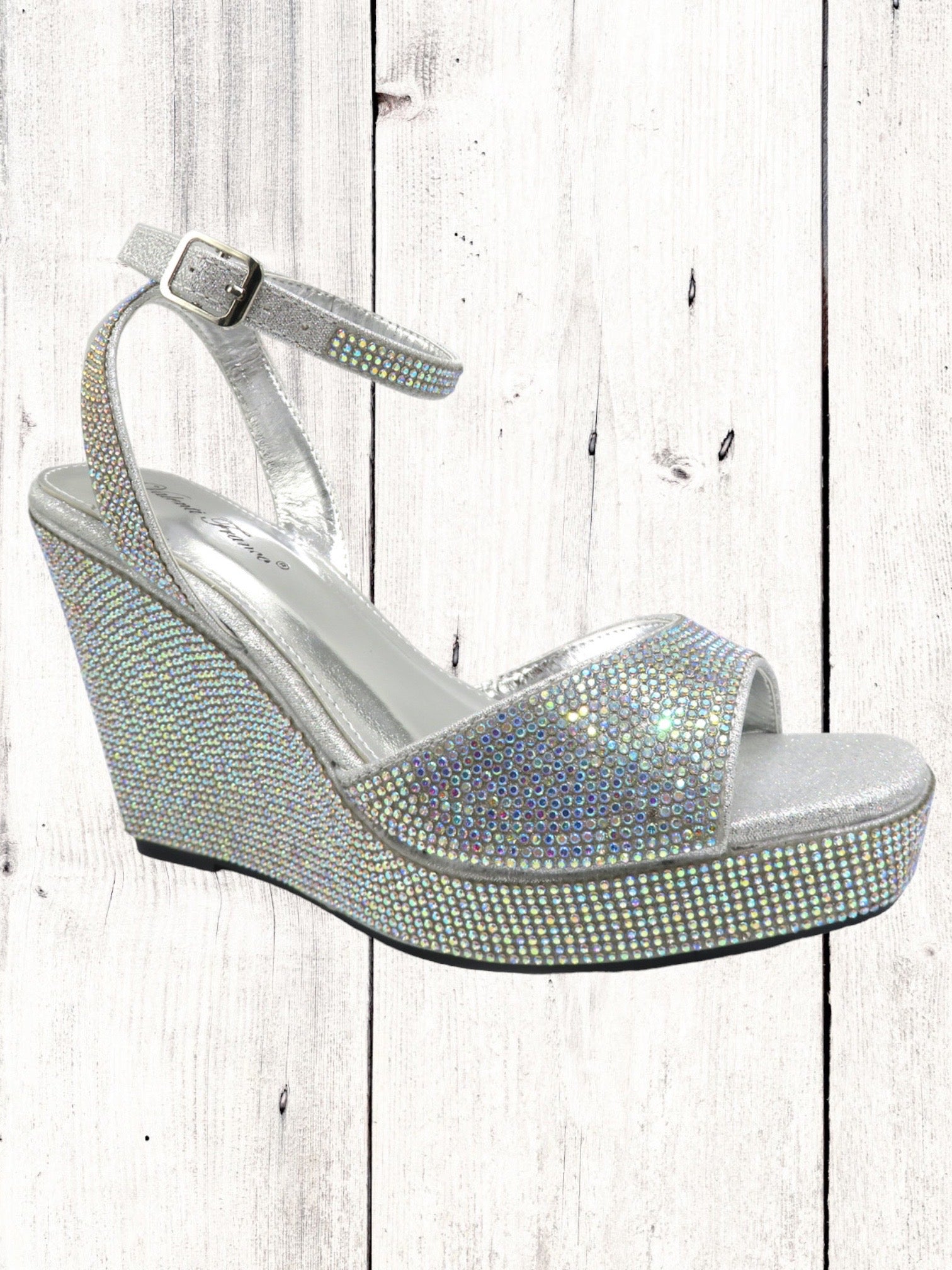 A silver-colored Valenti Franco Heart-1 wedge sandal with a rhinestone finish and an adjustable ankle strap, displayed against a wooden background.