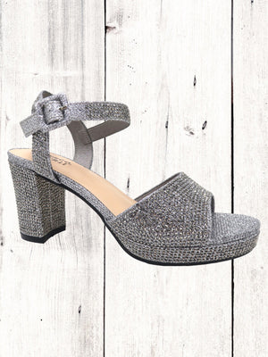 A black heel with a rhinestone design on the heel, featuring a one-strap design across the toe and an adjustable ankle strap on a white wooden surface.