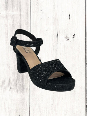A black heel with a rhinestone design on the heel, featuring a one-strap design across the toe and an adjustable ankle strap on a white wooden surface.