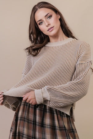 Woman wearing a beige sweater and plaid skirt against a beige background