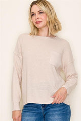 Woman wearing a beige sweater and blue jeans against a plain background