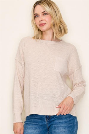Woman wearing a beige sweater and blue jeans against a plain background