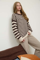 Woman wearing a striped sweater and beige pants against a white wall.