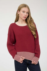 Woman wearing a red sweater with a striped hem against a white background