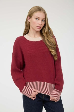Woman wearing a red sweater with a striped hem against a white background