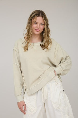 Woman wearing a beige sweater and white pants against a plain background