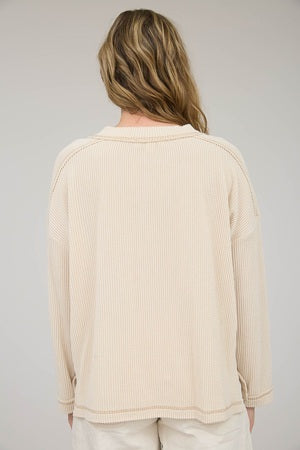 Woman wearing a beige ribbed sweater on a plain background