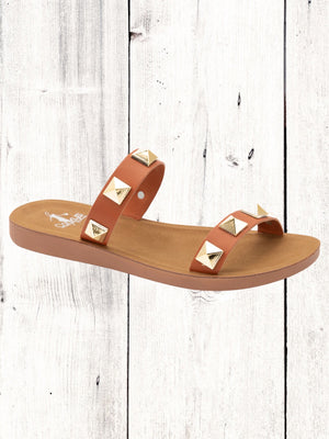 A black flat sandal with gold studs, featuring a comfortable fit and a brown sole.