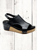 A black Corkys Volta II wedge sandal with a faux leather upper and cork wedge heel, featuring a hook and loop closure and studs on the heel.