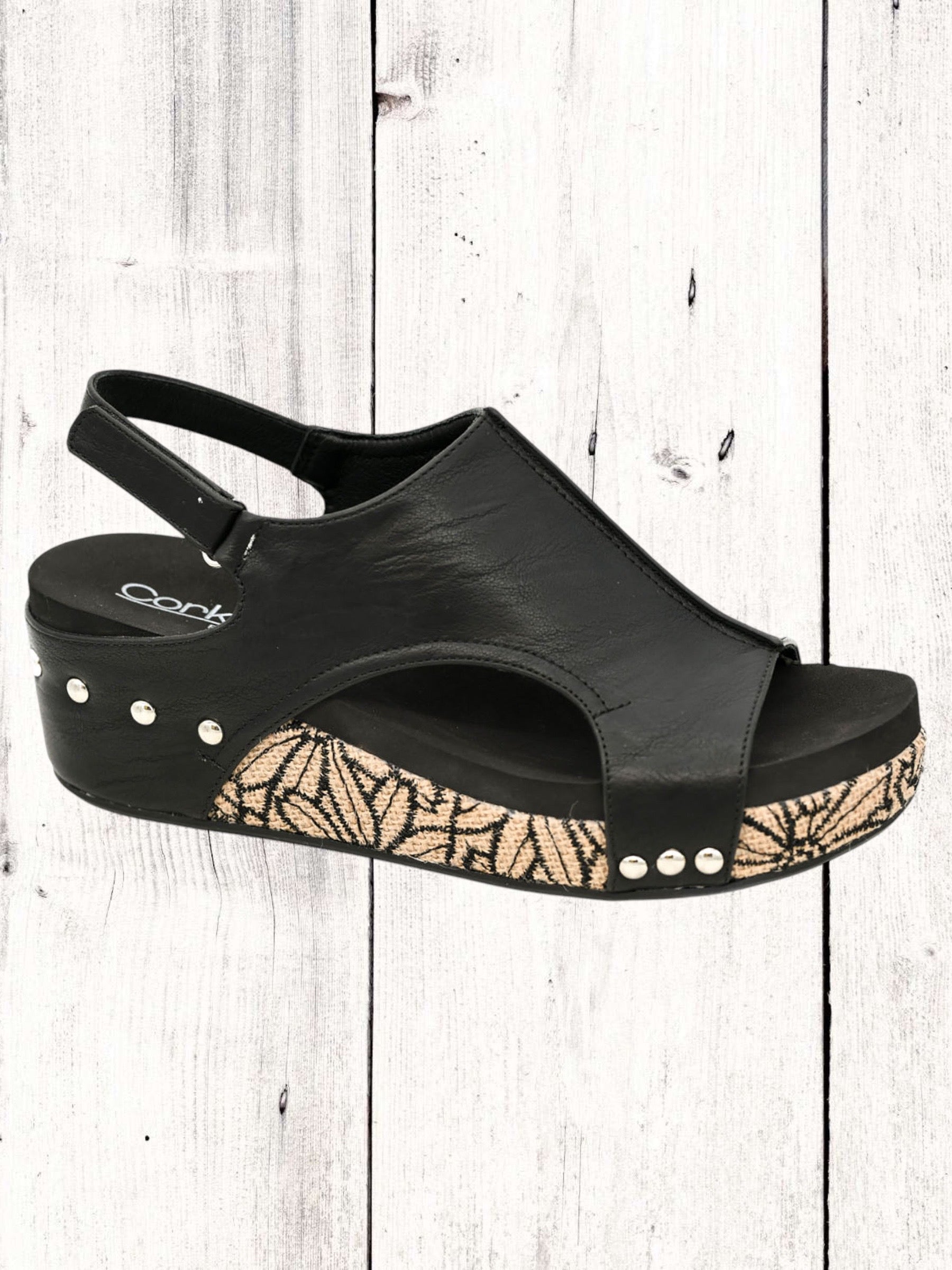 A black Corkys Volta II wedge sandal with a faux leather upper and cork wedge heel, featuring a hook and loop closure and studs on the heel.