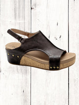 A black Corkys Volta II wedge sandal with a faux leather upper and cork wedge heel, featuring a hook and loop closure and studs on the heel.