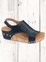 A black Corkys Volta II wedge sandal with a faux leather upper and cork wedge heel, featuring a hook and loop closure and studs on the heel.