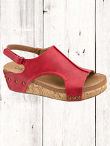 A black Corkys Volta II wedge sandal with a faux leather upper and cork wedge heel, featuring a hook and loop closure and studs on the heel.