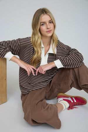 Woman wearing a brown striped sweater and brown pants sitting on the floor.