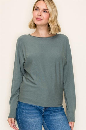 Woman wearing a green long-sleeve top and blue jeans against a white background