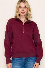 Woman wearing a burgundy sweater with a zipper on a plain background