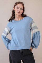 Woman wearing a light blue sweater with striped sleeves against a beige background