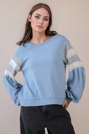 Woman wearing a light blue sweater with striped sleeves against a beige background