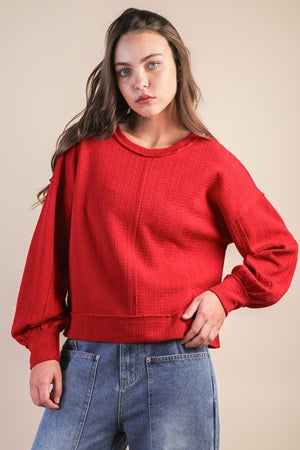 Person wearing a red sweater and blue jeans against a beige background