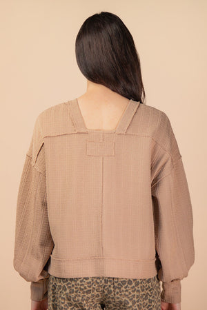 Person wearing a brown textured jacket on a beige background