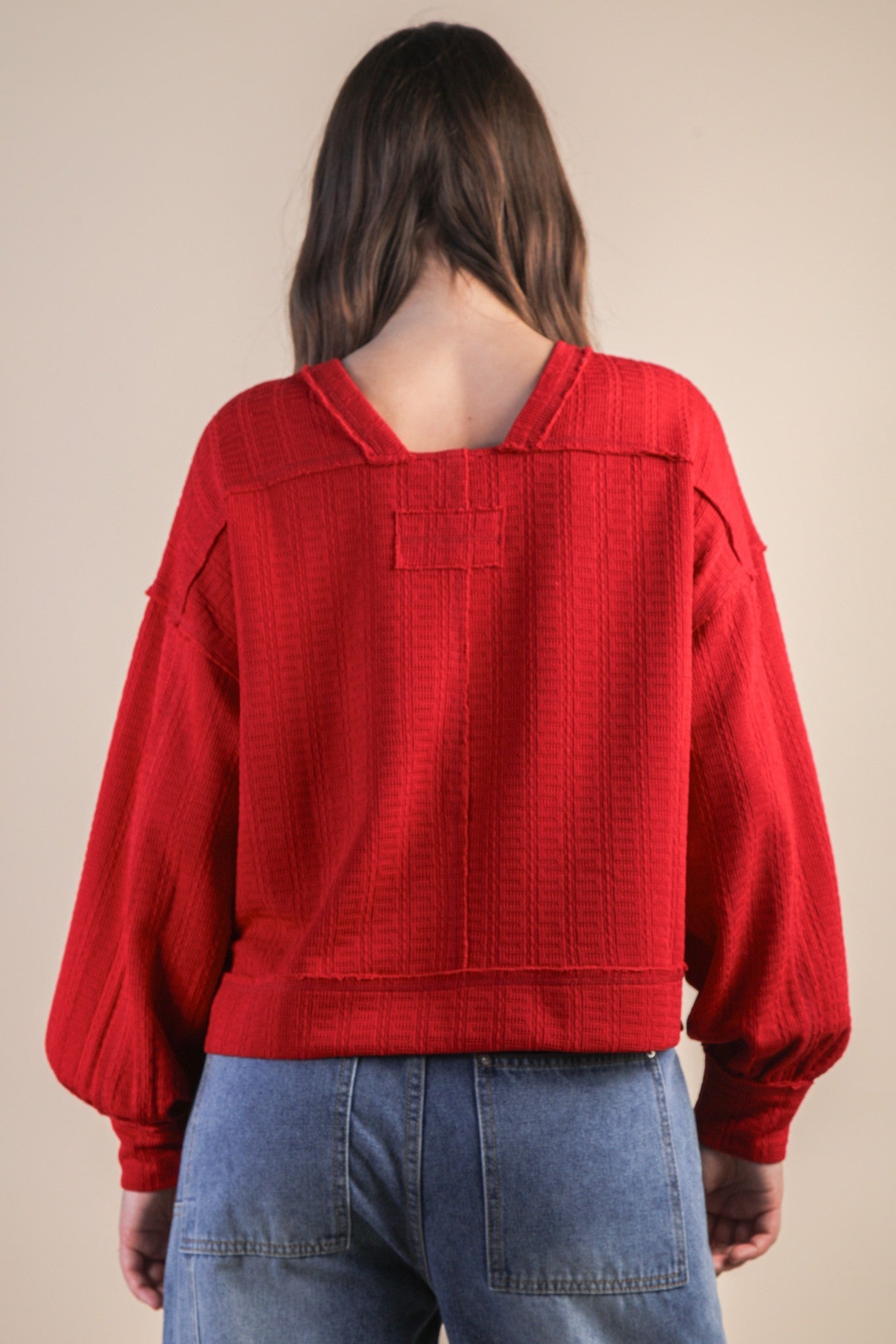 Person wearing a red textured sweater and blue jeans on a beige background