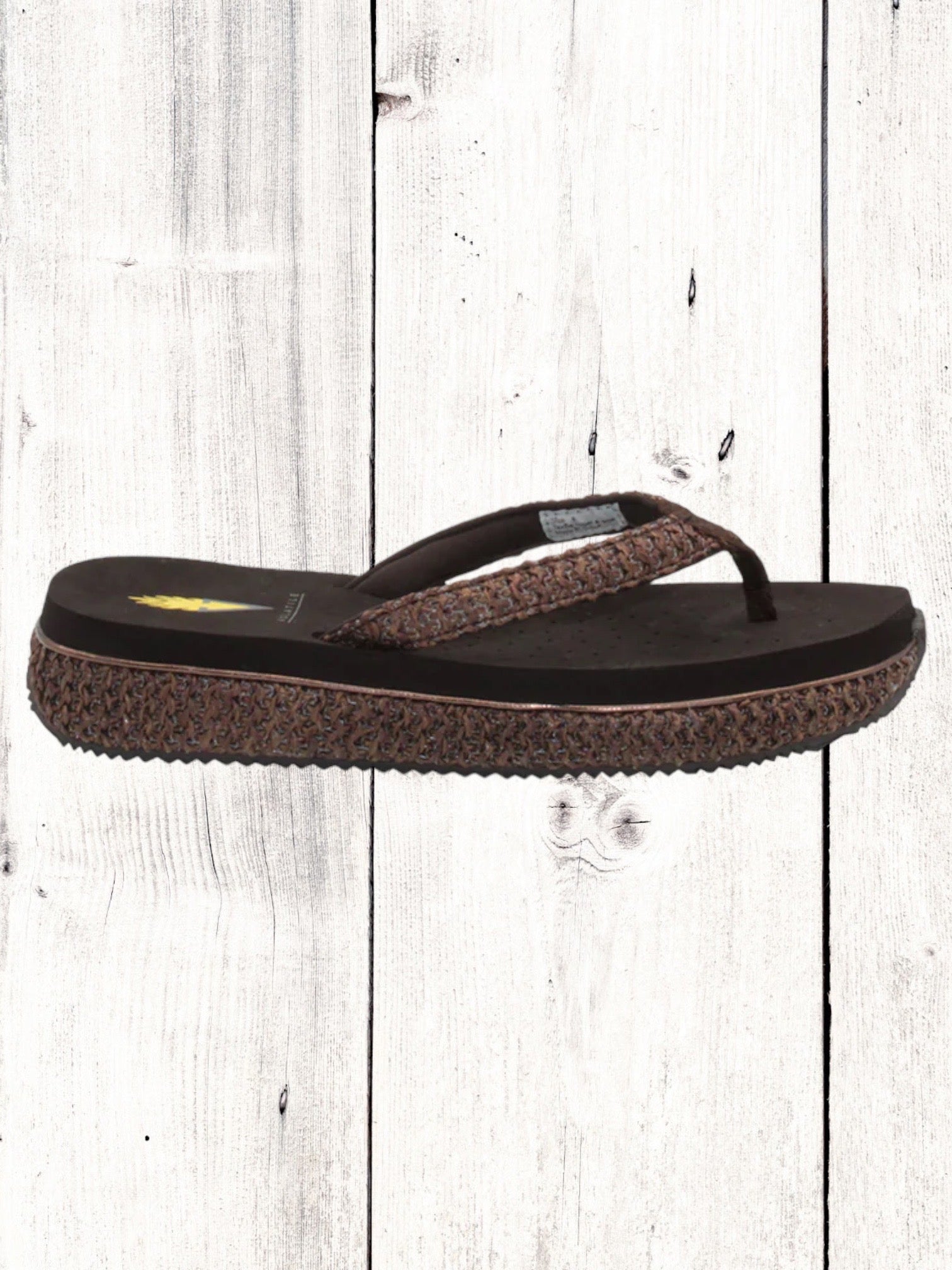 A pair of beige flip flops with a woven raffia upper and a low platform sole.