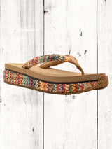 A pair of beige flip flops with a woven raffia upper and a low platform sole.
