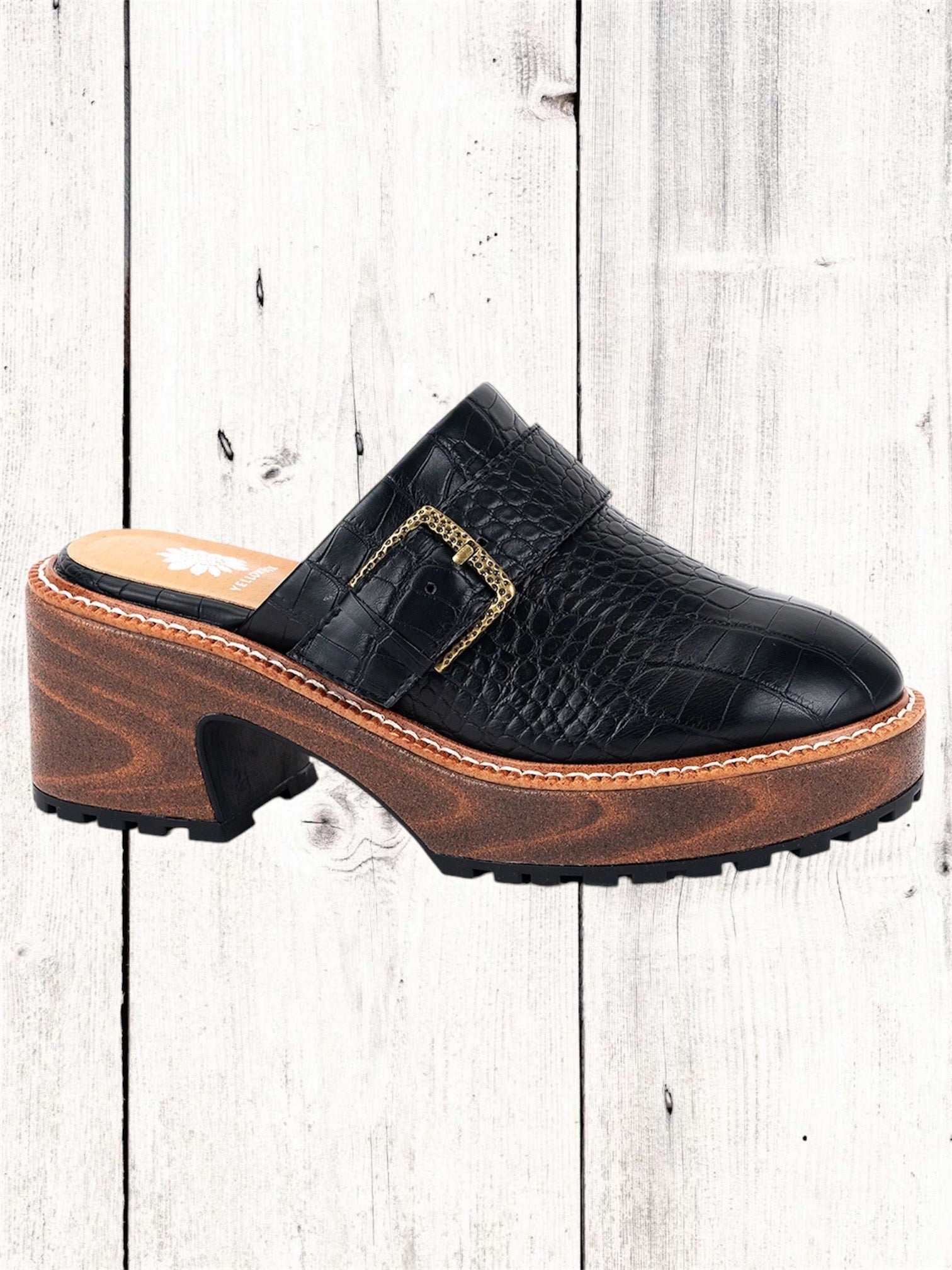 A black Yellow Box Barker Platform Clog with a wooden heel and a high rebound EVA footbed, displayed against a white wooden background.