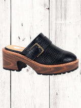 A black Yellow Box Barker Platform Clog with a wooden heel and a high rebound EVA footbed, displayed against a white wooden background.