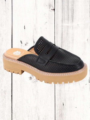 A black Yellow Box Sherlyn Mule featuring a perforated upper, chunky padded heel, and a lug outsole, set against a wooden backdrop.