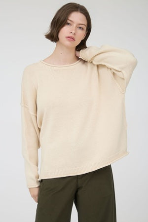 Woman wearing a beige sweater and dark pants against a white background