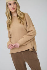 Woman wearing a beige sweater and brown pants against a white background