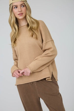 Woman wearing a beige sweater and brown pants against a white background
