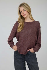 Woman wearing a maroon sweater and dark jeans against a plain background