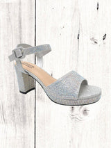 A black heel with a rhinestone design on the heel, featuring a one-strap design across the toe and an adjustable ankle strap on a white wooden surface.