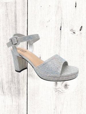 A black heel with a rhinestone design on the heel, featuring a one-strap design across the toe and an adjustable ankle strap on a white wooden surface.