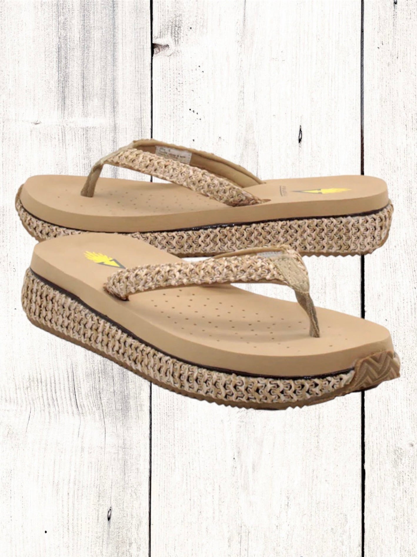 A pair of beige flip flops with a woven raffia upper and a low platform sole.