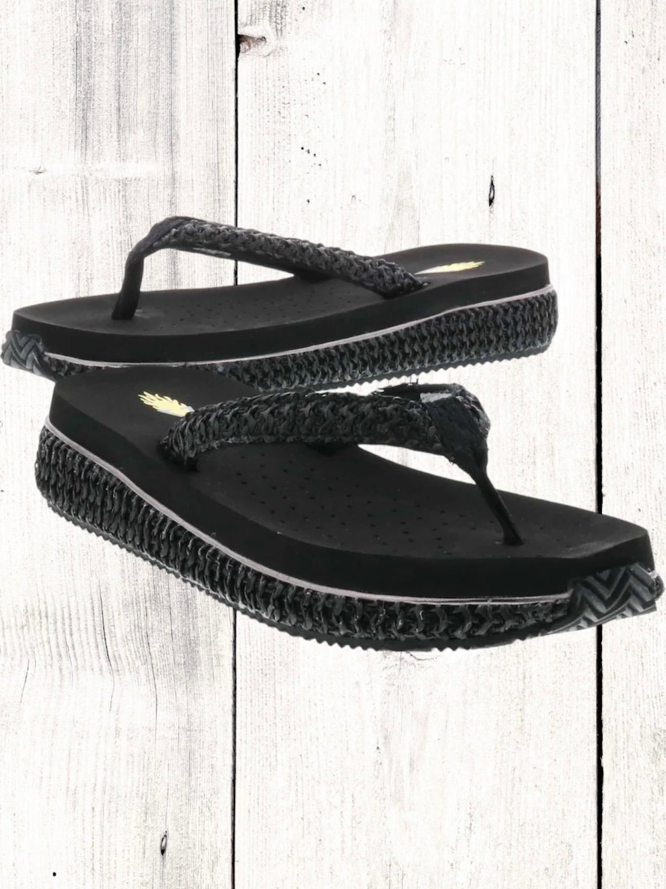 A pair of beige flip flops with a woven raffia upper and a low platform sole.