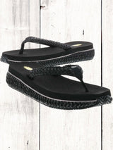 A pair of beige flip flops with a woven raffia upper and a low platform sole.
